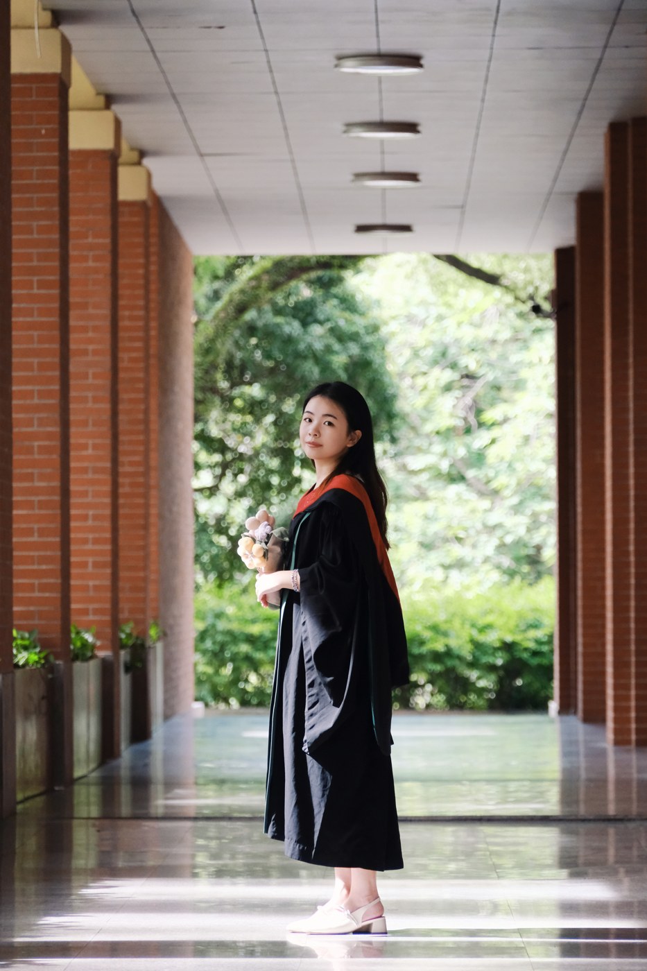 身穿学士服，站在校园廊道中的毕业照